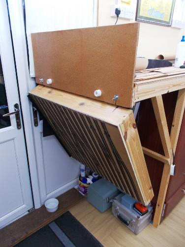 Prior to fitting of the layout’s green facias, the fold-down flap in front of one pair of external doors. 
The end board is to protect rolling stock when the flap is folded down out-of-use.
The hardwood cill underneath the cats water bowl protects two 37-way cables below.
www.EwhurstGreen.com 
